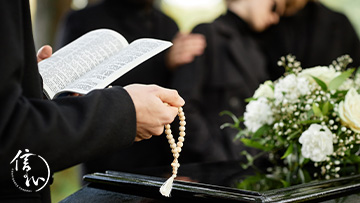 Close up of person in black praying at outdoor funeral and holding Bible with rosary, copy space