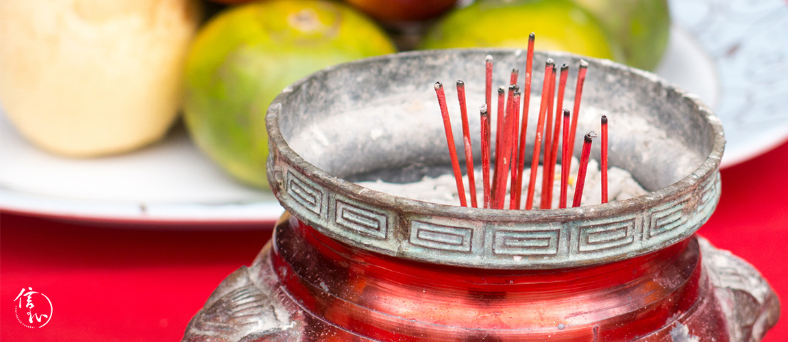 A red traditionally decorated bowl contains burnt incense sticks